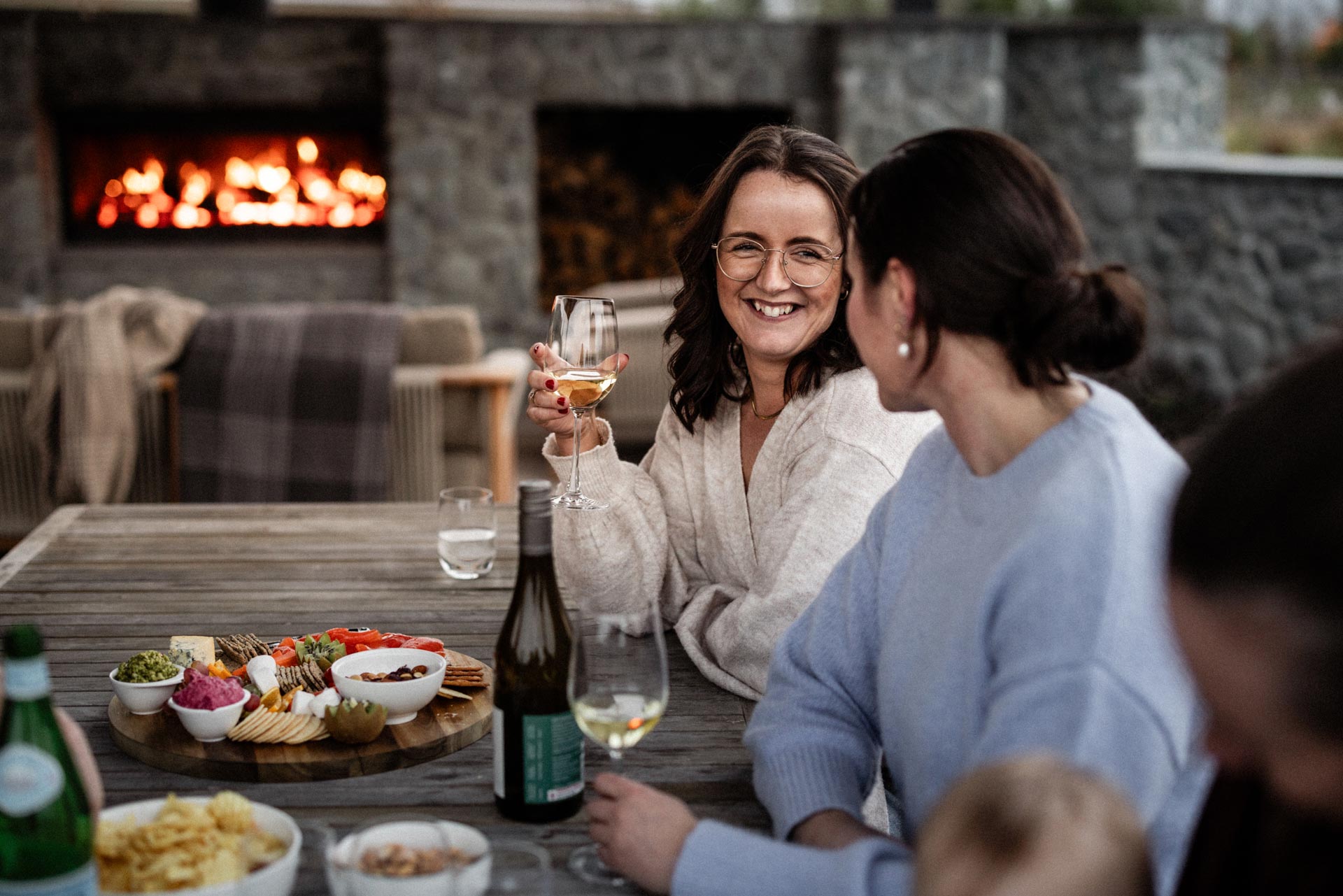 Friends sharing wine and a platter by the outdoor fireside at Whakahā